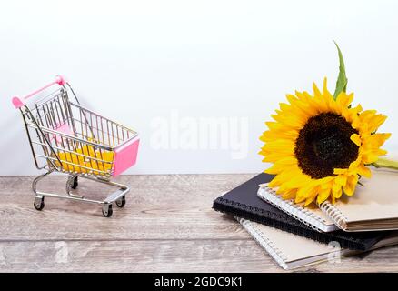 Sfondo della scrivania di ritorno alla scuola con una pila di libri di schizzo o di quaderni con bordo a spirale, cestino e girasole giallo, tema scolastico o educativo Foto Stock