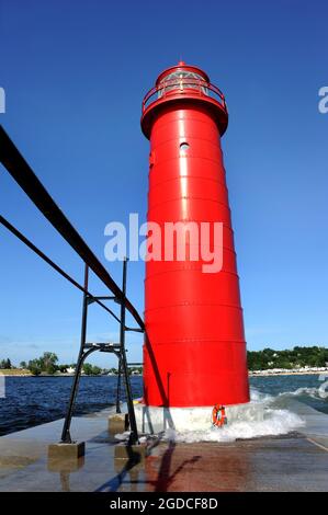 I cieli blu incorniciano il vivace faro rosso di Grand Haven sul lago Michigan. Le onde si lavano contro la base delle torri. Foto Stock