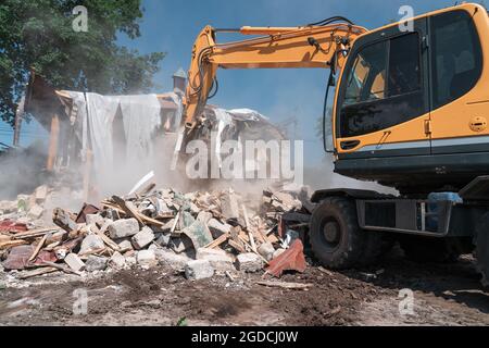 Demolizione di case. Il grande escavatore giallo interrompe la costruzione per una nuova costruzione. Foto Stock