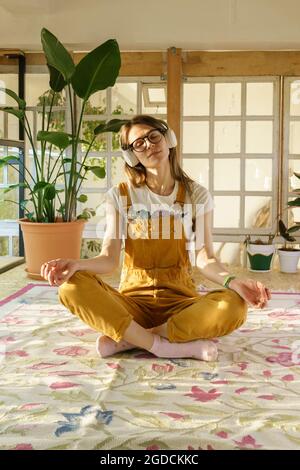 Giovane donna giardiniere meditate. Bella donna in tuta e cuffie rilassarsi dallo studio o dal lavoro Foto Stock