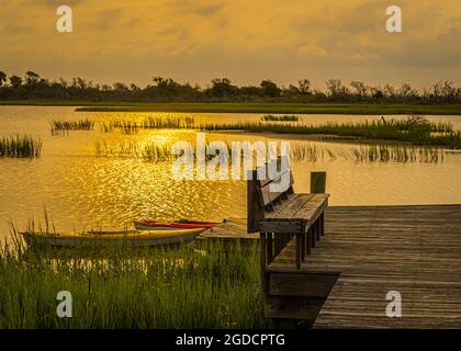 Golden mattina luce del sole su kayak vuoti legati ad un molo angolato di legno su una laguna isola. Foto Stock