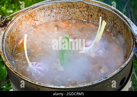 In acqua bollente, le teste di aglio e di pepe bollenti, coprendo in un calderone le carote a fette e i pezzi di carne nel processo di cottura del pilaf su una tradizione Foto Stock