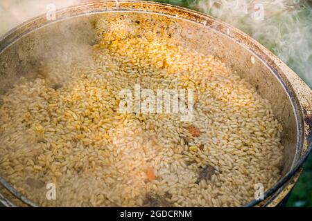 Riso in un calderone nel processo di cottura pilaf su un forno asiatico tradizionale. Ricetta passo-passo per pilaf reale. Foto Stock