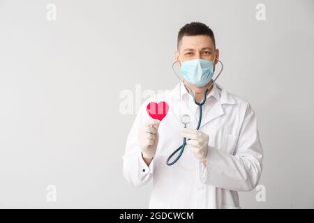 Cardiologo con cuore rosso e stetoscopio su sfondo chiaro Foto Stock