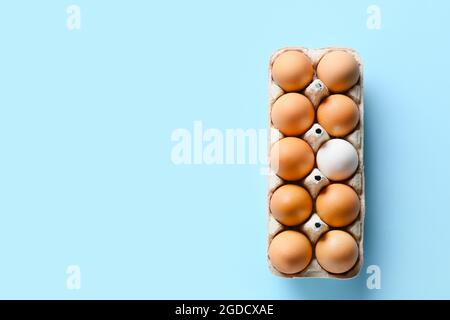 Scatola con uovo bianco tra quelli marroni su sfondo colorato. Concetto di unicità Foto Stock