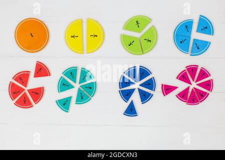 Frazioni multicolore, blocchi, taccuino su tavola di legno bianco. Ritorno a scuola, matematica divertente, giochi per l'asilo, istruzione prescolare. Foto Stock