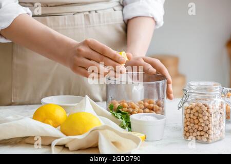 Donna spremitura limone in frullatore con ceci sul tavolo in cucina, primo piano Foto Stock