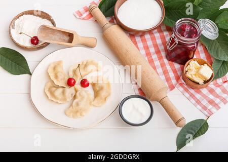 Composizione con gustosi gnocchi di ciliegia e salsa su sfondo di legno chiaro Foto Stock