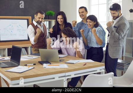 Team di persone che lavorano con piacere che guardano allo schermo del notebook e festeggiano l'affare di successo Foto Stock
