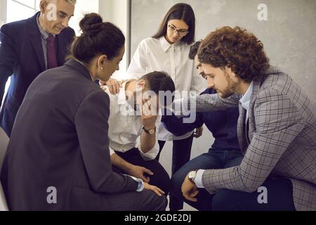 Gruppo di amici o colleghi che conforta il giovane triste che nasconde il suo volto e piange Foto Stock