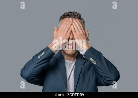 Uomo in giacca che ricopre il viso con palme Foto Stock