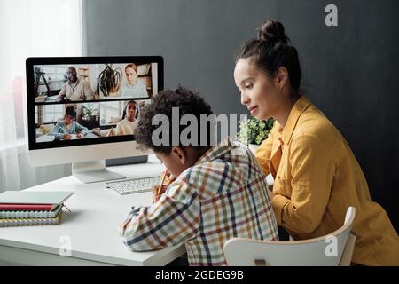 Madre che aiuta suo figlio a fare i compiti al tavolo durante la conversazione online sul computer Foto Stock