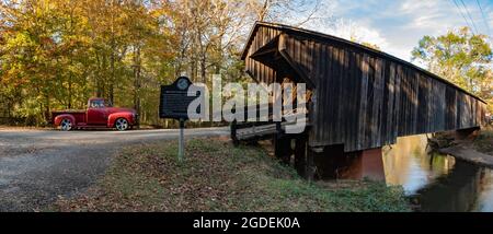 Woodbury, Georgia, USA- 14 novembre 2020: Banner web panoramico di un camion rosso d'epoca accanto allo storico Red Oak Creek Covered Bridge. Alcuni dicono che è t Foto Stock