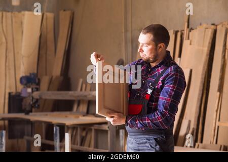 il falegname nei vestiti di lavoro guarda un proprio prodotto Foto Stock