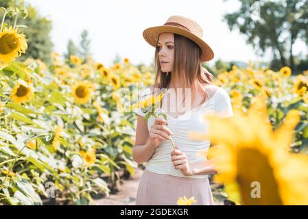 bella ragazza dolce in un cappello di paglia che cammina su un campo di girasoli , sorridente Foto Stock