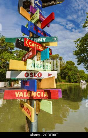 Carcassonne, Francia. Posta con cartelli che indicano la direzione di varie città del mondo con diversi colori sul Canal du Midi Foto Stock