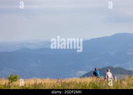 Feldberg, Germania. 13 Agosto 2021. I turisti camminano lungo un sentiero vicino alla cima del Feldberg, mentre sullo sfondo si possono vedere le nebbie pendii della Foresta Nera. La Foresta Nera è ancora una delle destinazioni turistiche più famose dell'entroterra. Credit: Philippe von Ditfurth/dpa/Alamy Live News Foto Stock