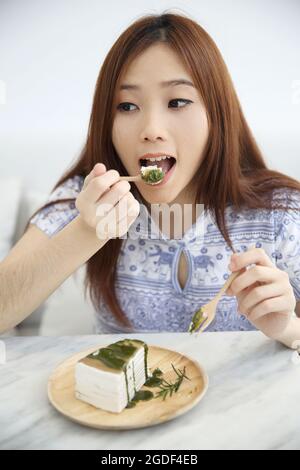 Giovane donna asiatica mangiare tè verde torta di ravizzone cibo dolce Foto Stock