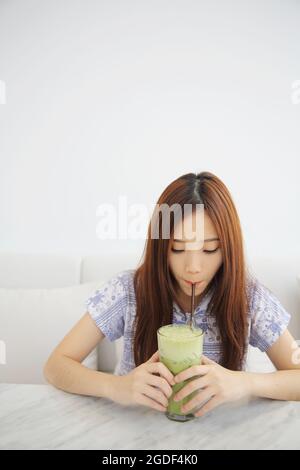 Giovane donna asiatica che beve latte di tè verde freddo in coffeeshop bianco Foto Stock