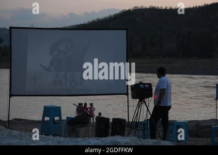 (210813) -- TAIYUAN, 13 agosto 2021 (Xinhua) -- Xue Xiaogang (L) regola i dispositivi di proiezione del film dal fiume giallo nella città di Sanjiao della contea di Liulin, la provincia di Shanxi della Cina del nord, 14 luglio 2021. Nel 1975, Sanjiao Township fondò un team di proiezione cinematografica. Liu Bufei e Liu Dengzhao, entrambi cinefili fin dall'infanzia, si unirono alla squadra e divennero proiettisti rurali. Nel 2007, la squadra divenne una troika con l'ingresso del proiettile di seconda generazione Xue Xiaogang, che aveva visto film all'aperto nel villaggio mentre era cresciuto. Nel corso degli anni, il team di proiezione, per innumerevoli volte ha Foto Stock