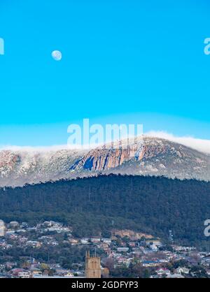 Con la luna ancora su una coperta di nuvola di mattina presto rotola sopra Kunanyi (Monte Wellington) verso Hobart, la capitale della Tasmania in Australia Foto Stock