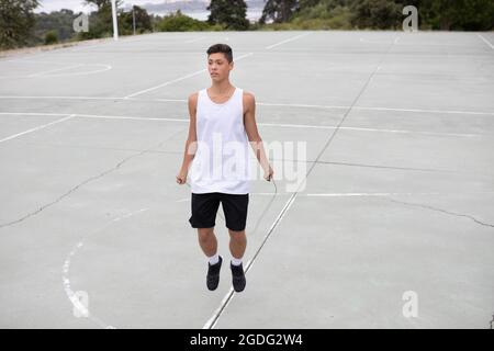 Un adolescente di sesso maschile del giocatore di basket sul campo da pallacanestro saltando Foto Stock