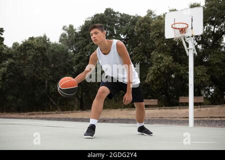 Un adolescente di sesso maschile del giocatore di basket giocare a basket su corte Foto Stock