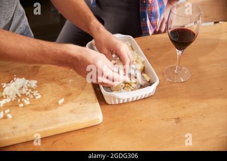 Paio di mettere le verdure nella tostatura piatto sul tavolo da cucina, close up delle mani Foto Stock