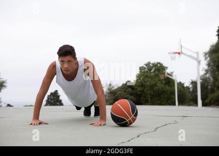 Un adolescente di sesso maschile del giocatore di basket sul campo da pallacanestro facendo ups push Foto Stock