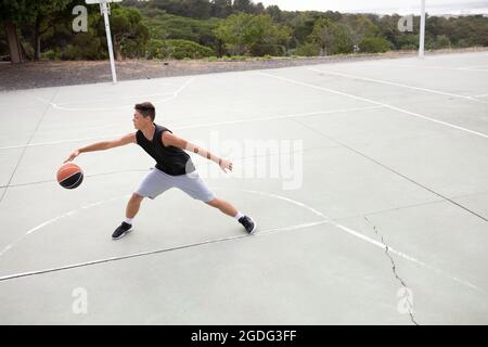 Un adolescente di sesso maschile del giocatore di basket la pratica sul campo di pallacanestro Foto Stock