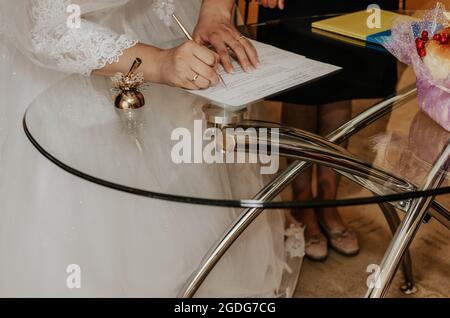 Mano umana con scrittura pen.Official cerimonia nuziale in registro office.bride e sposo lasciare la loro firma sul modulo sul tavolo. Sposi si consolidano Foto Stock