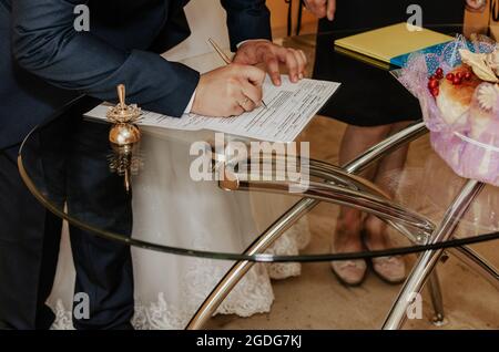 Mano umana con scrittura pen.Official cerimonia nuziale in registro office.bride e sposo lasciare la loro firma sul modulo sul tavolo. Sposi si consolidano Foto Stock