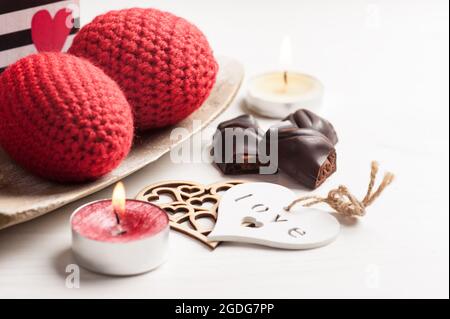 Composizione di candela illuminata rossa frizzante e cioccolato fondente per San Valentino su tavolo bianco shabby. Foto Stock