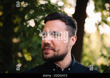Primo piano ritratto di uomo felice sicuro in piedi contro gli alberi in estate Foto Stock