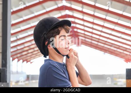 Ragazzo adolescente che mette un casco da cavalcare sulla testa. Foto Stock