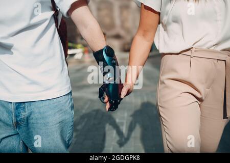 Giovane uomo disabile con mano protesica artificiale che cammina e tiene la mano della ragazza della donna Foto Stock