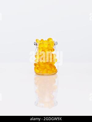 Capsule di gelatina di olio di pesce, gialle, in flacone di vetro su tavola bianca con riflessione. Compresse di vitamina capsule. Industria farmaceutica. Naturale, immu Foto Stock