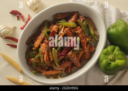 Baby mais manchurian. Croccante mais fritto in salsa manchuriana con peperoni e cipolle. Scatto su sfondo bianco Foto Stock