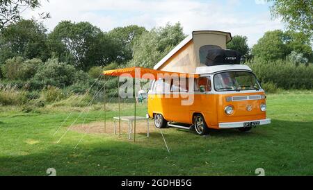 Classic Orange Volkswagen Camper Van parcheggiato sul campo Site dal fiume con il rabbocco e la tenda . Foto Stock