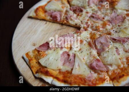 pizza hawaiana, pizza con ananas e prosciutto con salsa di formaggio e pomodori su fondo di legno, cibo italiano Foto Stock