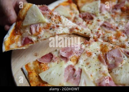 pizza hawaiana, pizza con ananas e prosciutto con salsa di formaggio e pomodori su fondo di legno, cibo italiano Foto Stock