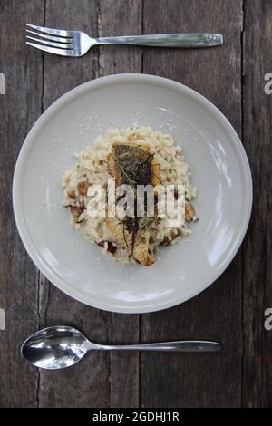 risotto con filetto di branzino su fondo di legno, cucina italiana Foto Stock