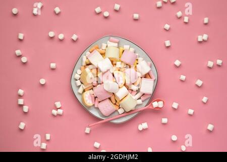 Marshmallow colorati su una piastra quadrata bianca isolata su sfondo rosa. Marshmallows sparsi. Primo piano della texture di un morbido marshmallow. Foto Stock