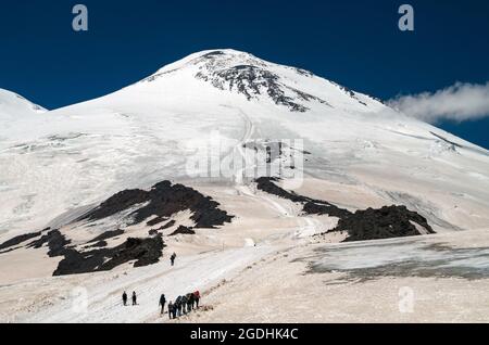 Gli arrampicatori vanno in cima al Monte Elbrus.UN gruppo di turisti con zaini, camminando uno dopo l'altro, sale fino alla cima della montagna su una neve-insenatura Foto Stock