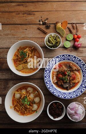 Cibo locale della Tailandia del nord: Porcini all'uovo al curry con pollo e polpette e tagliatelle di riso su sfondo di legno Foto Stock