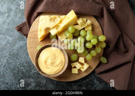 Tavola con salsa al formaggio, uva e formaggio su tavolo nero fumé con asciugamano da cucina Foto Stock