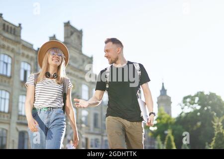 Due studenti allegri, maschi e femmine, con zaini che sollevano i pollici al campus universitario tenendo un laptop. Adorabile coppia di studenti di successo sorridendo mostrando i pollici fino segno alla fotocamera Foto Stock