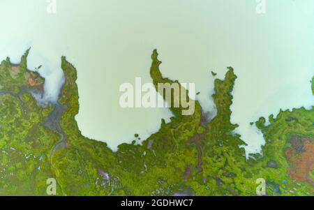 Vista sul drone delle acque nuvolose del lago situato vicino alla costa verde mussosa nella campagna dell'Islanda Foto Stock