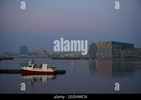 Nave ormeggiata vicino al molo nel quartiere costiero della città moderna al tramonto in Islanda Foto Stock