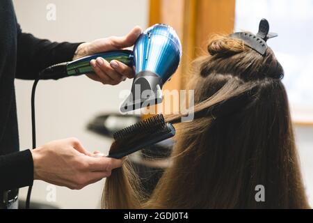 Master donna parrucchiere asciuga i capelli della ragazza con un asciugacapelli e pettini dopo il lavaggio nel salone di bellezza Foto Stock